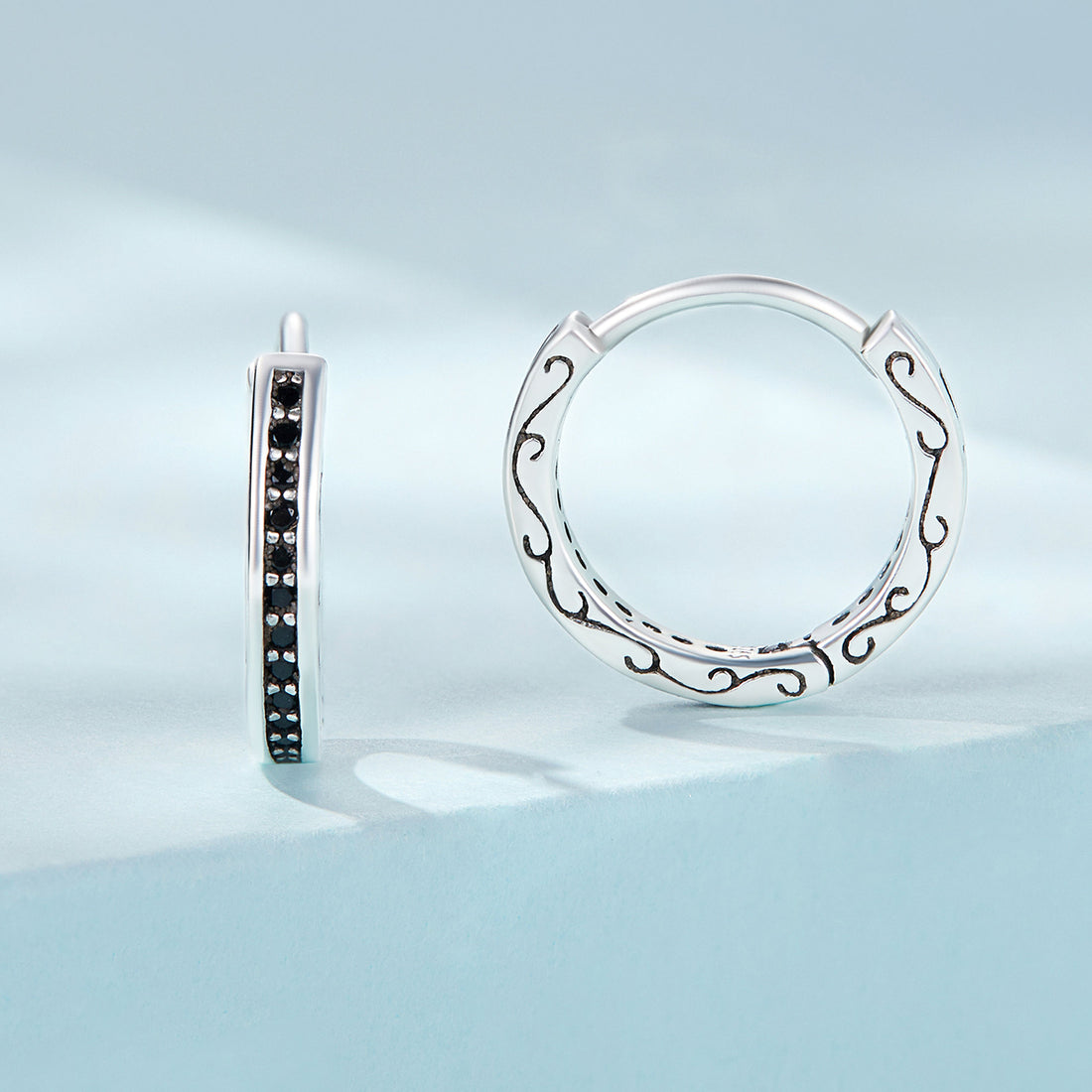Pair of silver hoop earrings with black gemstones on a white background
