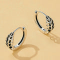 Pair of silver hoop earrings with leaf design on a beige background