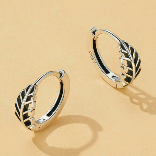 Pair of silver hoop earrings with leaf design on a beige background