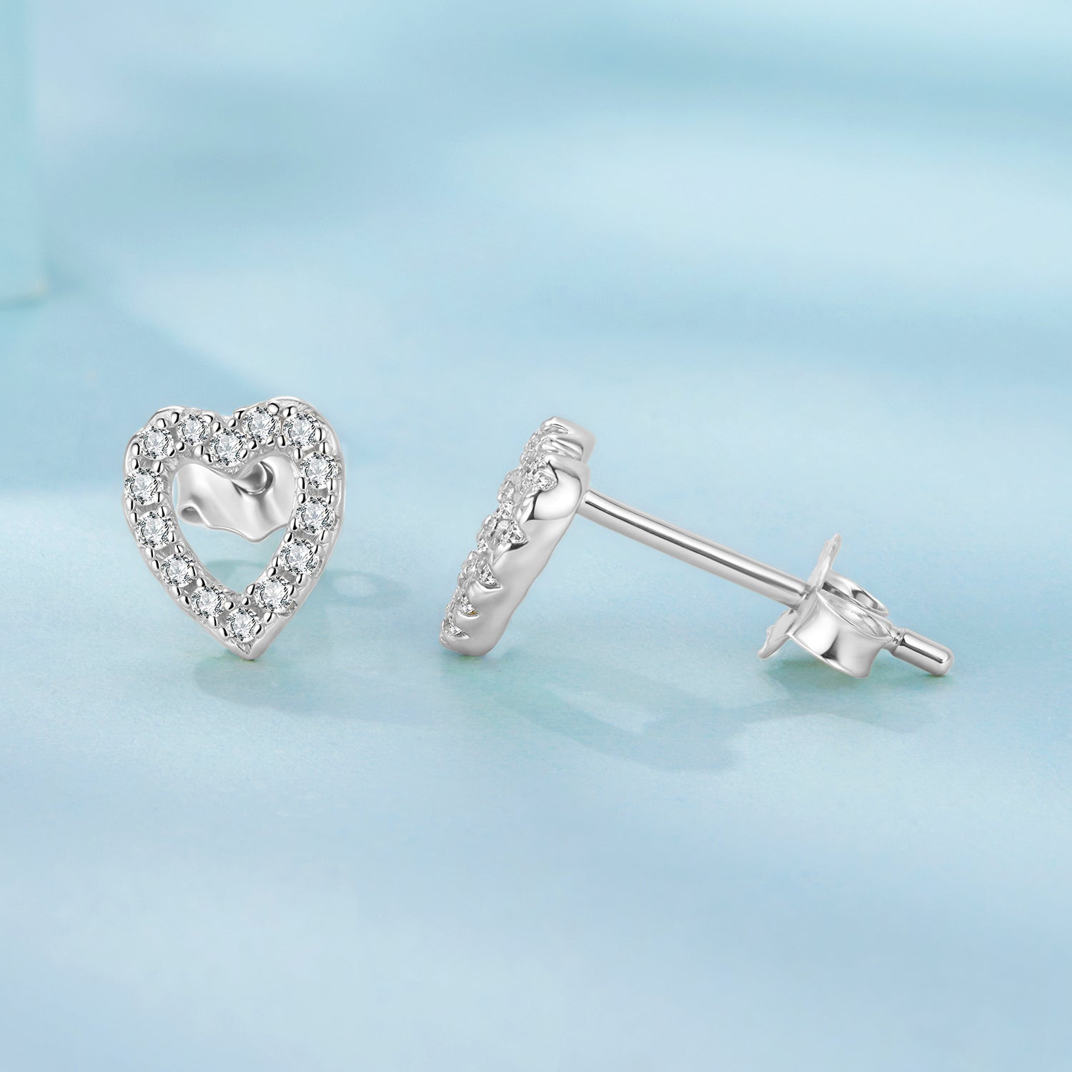 Heart-shaped silver earrings on a light blue background