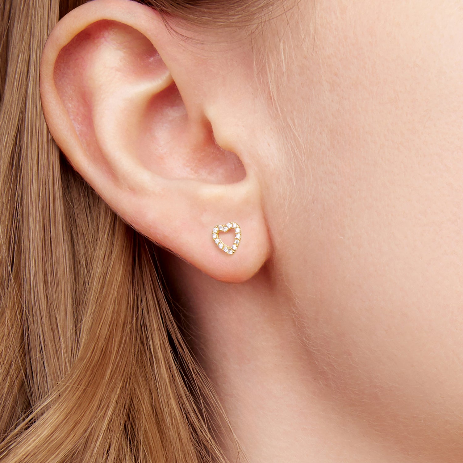 Heart-shaped earring worn by a person with blonde hair.