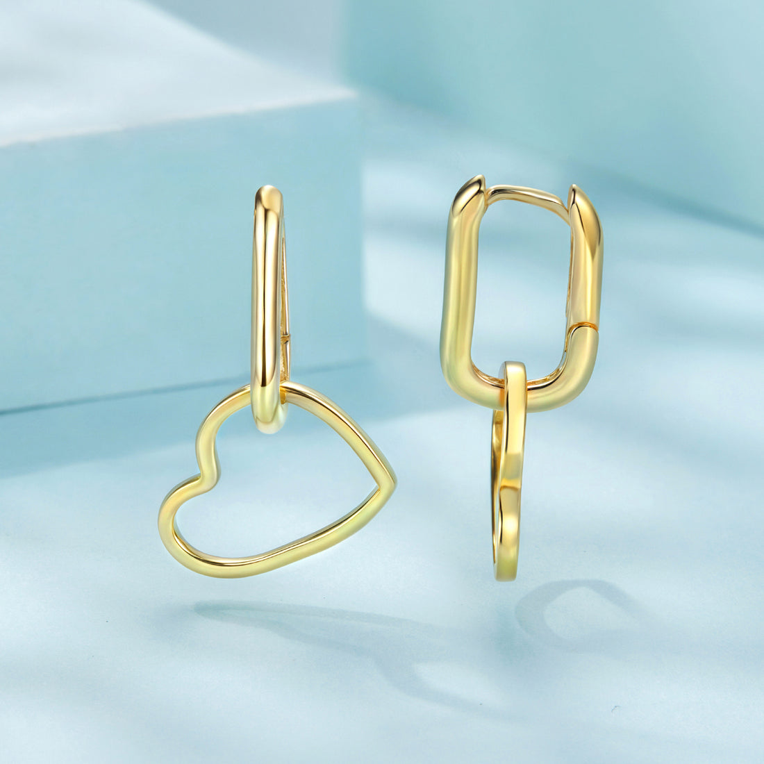 Gold heart-shaped earrings on a light blue background