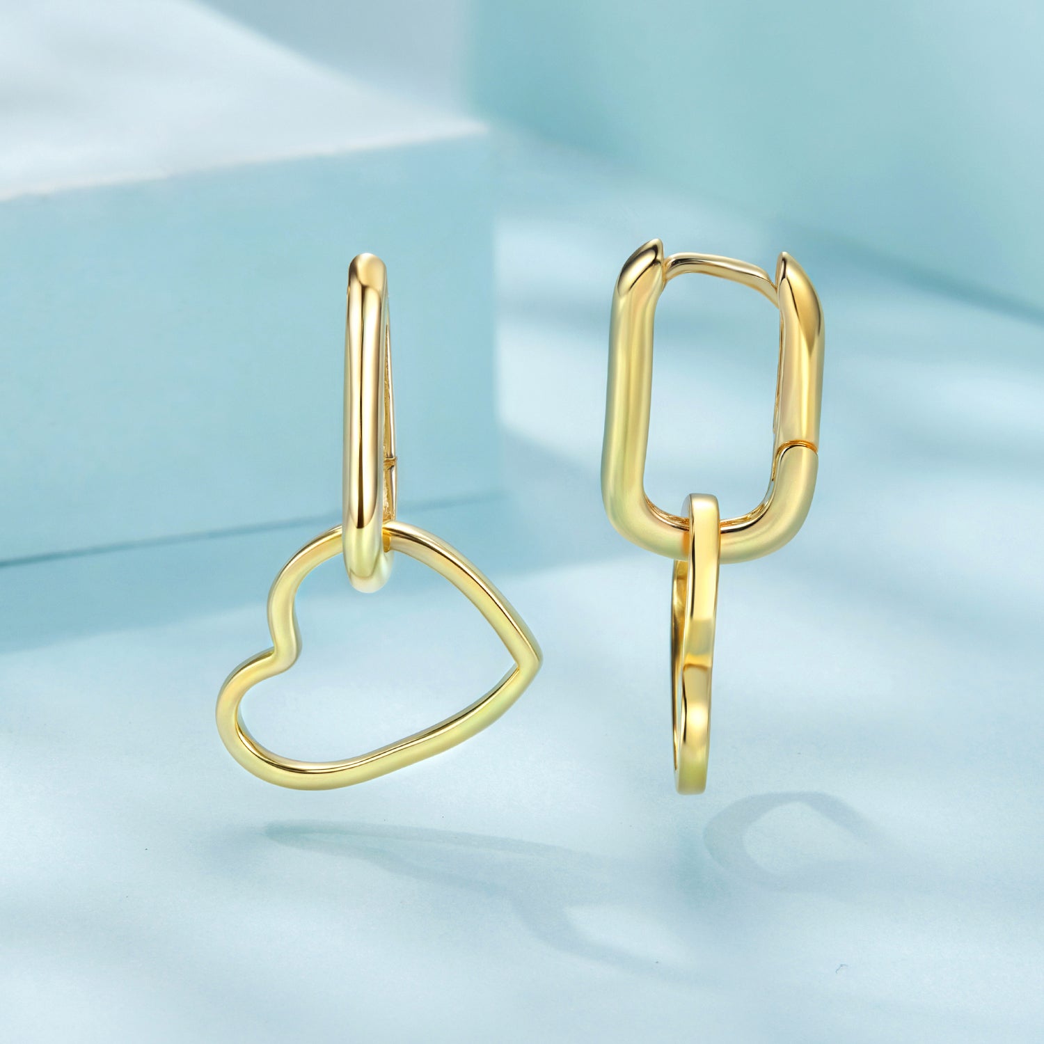 Gold heart-shaped earrings on a light blue background