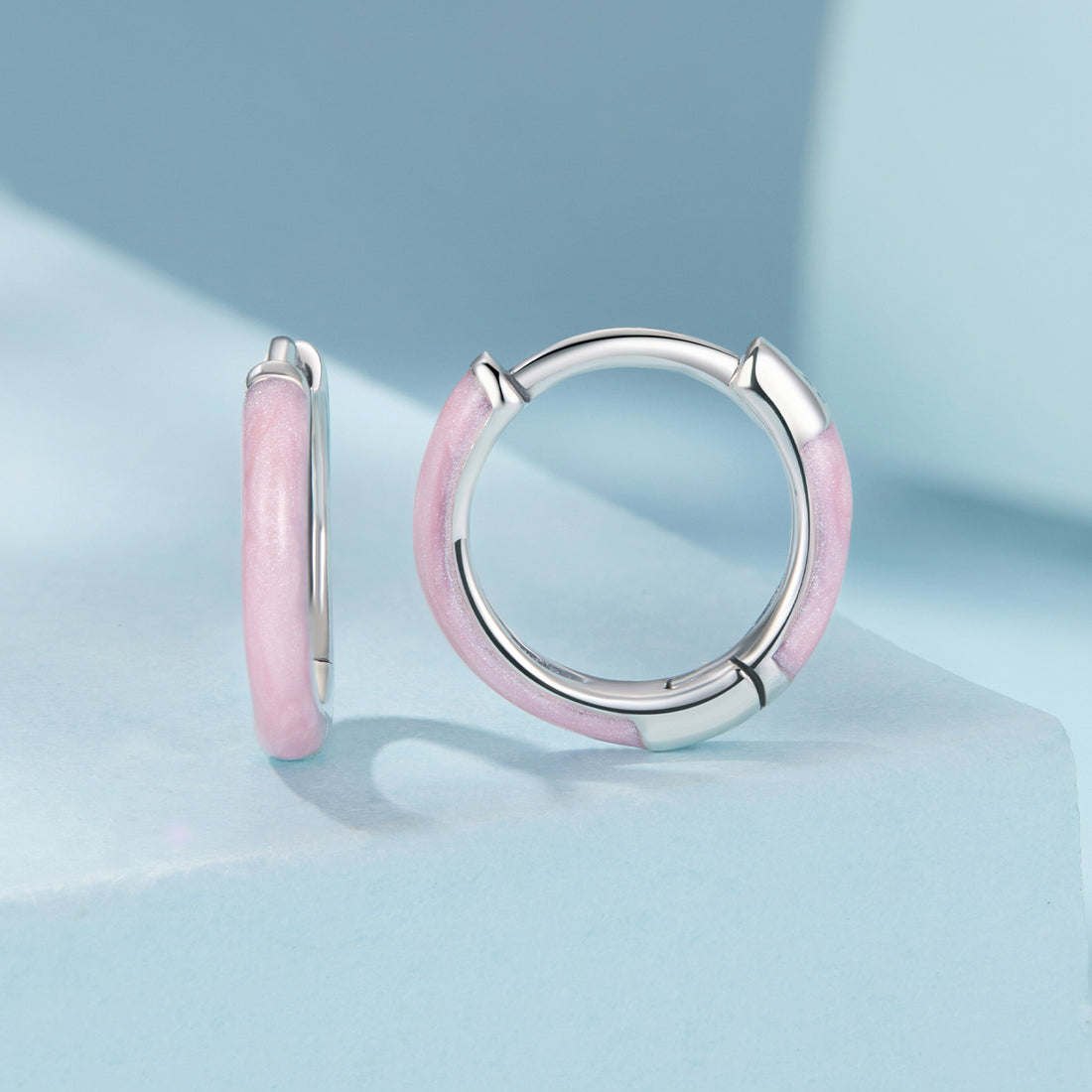 Pink hoop earrings with silver accents on a light blue background