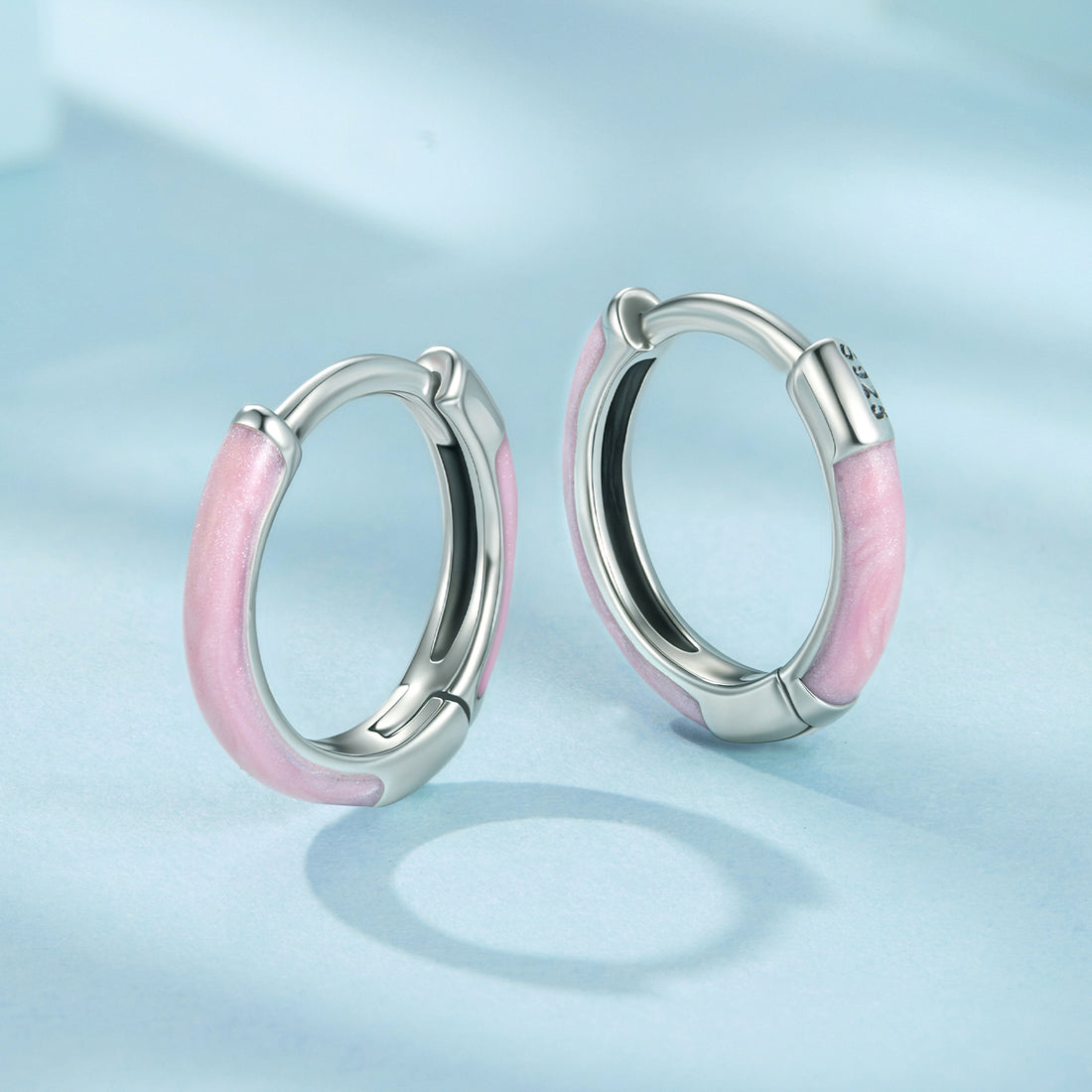 Pink hoop earrings with silver accents on a light blue background