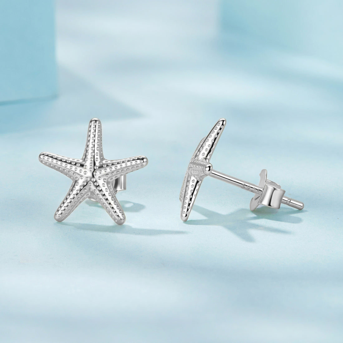 Starfish-shaped silver earrings on a light blue background