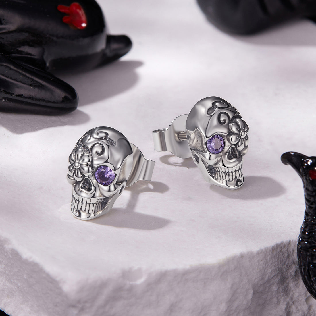 Silver skull earrings with purple gemstones on a white background