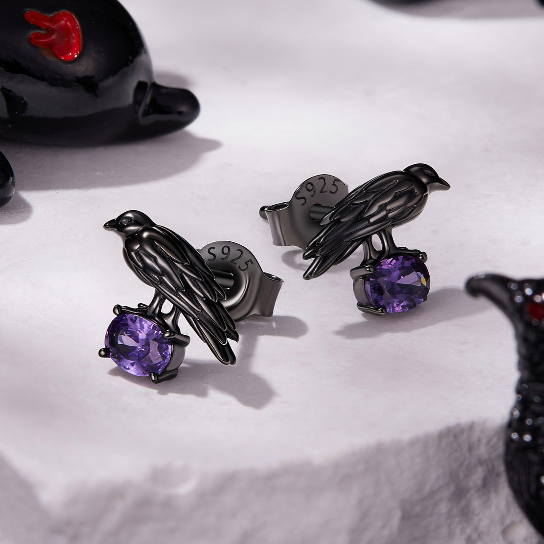 Black bird-shaped earrings with purple gemstones on a white background