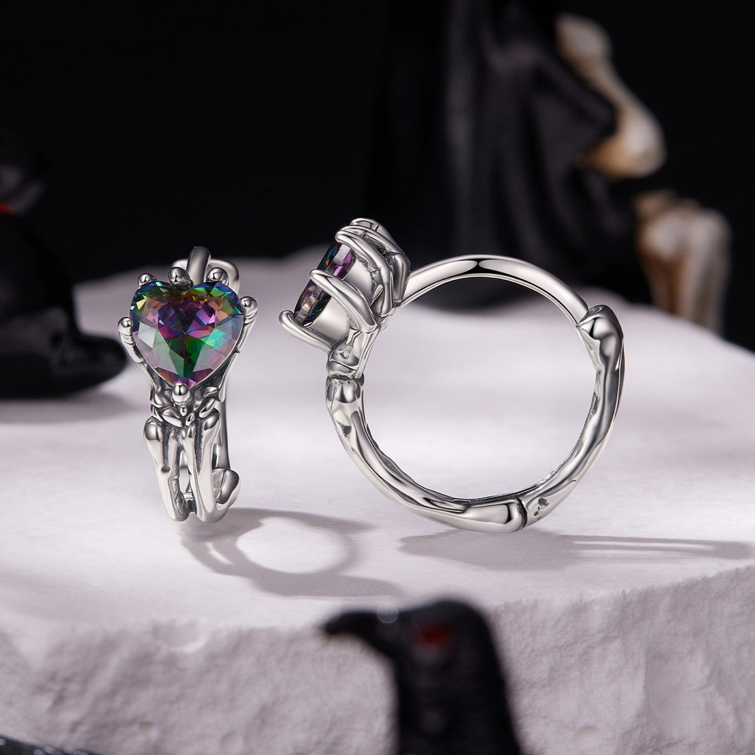 Pair of silver hoop earrings with heart-shaped multicolored gemstones on a white background