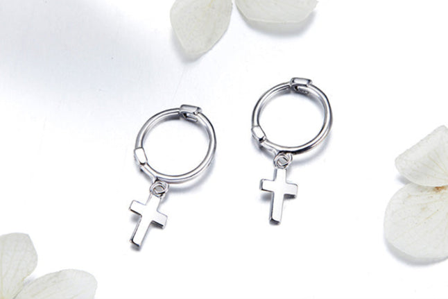 Silver hoop earrings with cross charms on a white background with flowers.