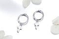 Silver hoop earrings with cross charms on a white background with flowers.