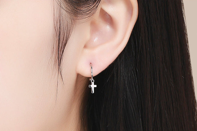 Silver hoop earrings with cross charms on a white background with flowers.