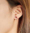Close-up of an ear wearing a red and silver earring with hair partially obscuring the view.