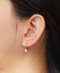 Close-up of an ear wearing a silver hoop earring with a small pearl.