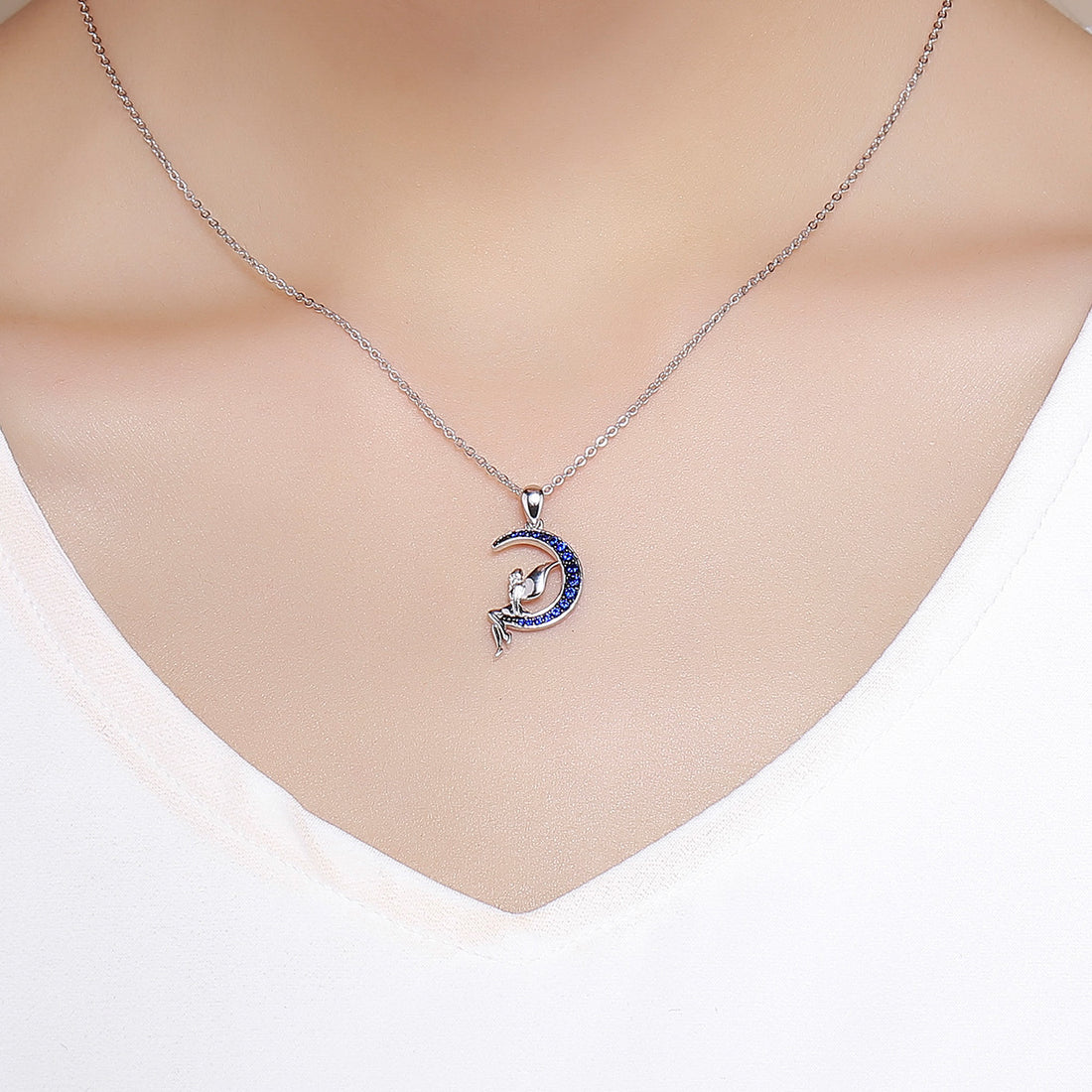 Silver necklace with a moon and fairy pendant featuring blue stones on a white background