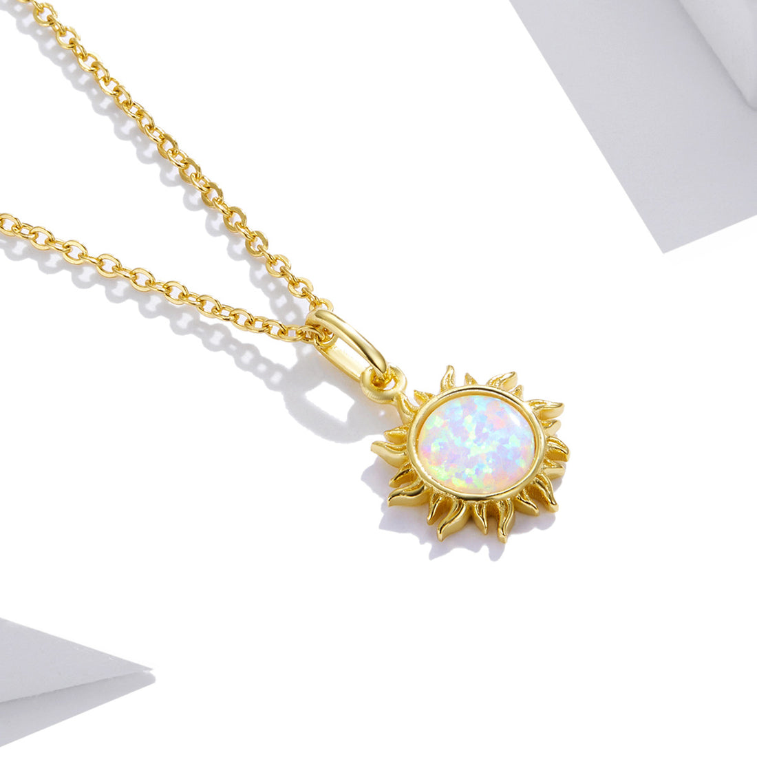 Gold necklace with a sun-shaped pendant featuring an opal stone on a light gray background
